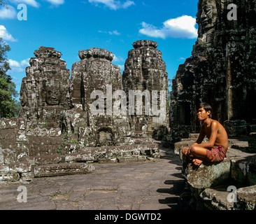 Temple Bayon, l'homme assis sur la deuxième terrasse, face à tours, les visages de sourire d'Avalokiteshvara, Bodhisattva Lokeshvara Banque D'Images