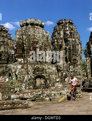 Temple Bayon, l'homme avec un balai à travailler sur la deuxième terrasse, face à tours, les visages souriants de Bodhisattva Lokeshvara Banque D'Images