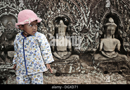 Enfant debout en face de Bouddha stone carvings, Angkor Wat, Siem Reap, Cambodge, Asie Banque D'Images