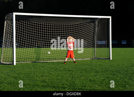 Petit garçon de cinq ans portant une robe de football FC Bayern Munich, boredly debout dans un but de soccer Banque D'Images