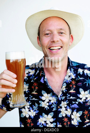 Smiling homme portant un chapeau de paille et une chemise hawaïenne tenant une bière de blé Banque D'Images