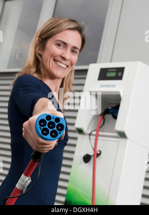 Femme tenant un bouchon de charge pour une voiture électrique, debout devant une accusation CP700d'une station de charge de Siemens, Fürth Banque D'Images