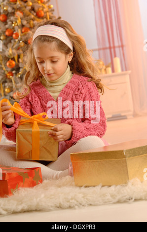 Déballage de fille un cadeau en face d'un arbre de Noël Banque D'Images