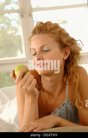 Femme blonde, 25-35 ans, est calé sur son ventre au lit holding an apple Banque D'Images