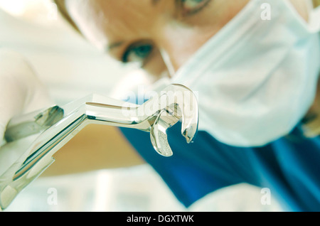 Dentiste portant un masque de visage et la tenue d'une pince pour arracher des dents Soins dentaires Banque D'Images