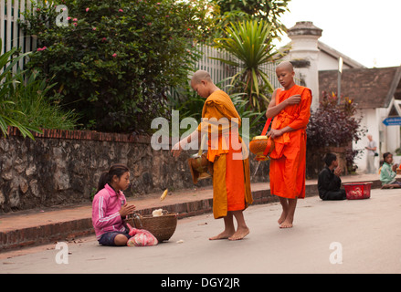 Un moine bouddhiste donne une pauvre fille nourriture pendant la cérémonie quotidienne du matin de l'aumône aux moines à Luang Prabang, Laos. Banque D'Images