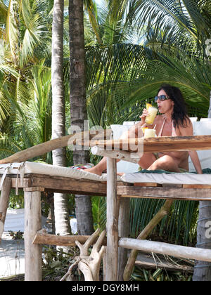 Femme, 45, de boire un cocktail sur un siège surélevé à un bar de plage sous les palmiers, Playa Samara, Péninsule de Nicoya, Costa Rica Banque D'Images