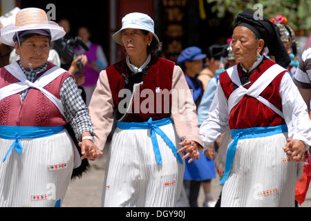 Trois femmes en costume traditionnel de la minorité Naxi tenant la main et dansant sur la place principale de Lijiang, Yunnan Banque D'Images