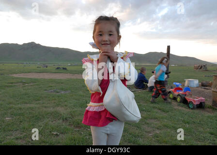 Fillette de 5 ans avec un sac blanc et rouge de l'article robe et souriant devant des enfants jouant dans les prairies à la Banque D'Images