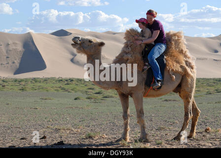 Jeune femme avec foulard rouge assis avec une fille de quatre ans sur un chameau blanc devant les grandes dunes de sable Khorgoryn Els dans le Banque D'Images