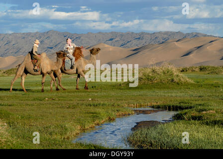 Les touristes sur les chameaux chameau mongol avec butée de guidage à l'eau les chameaux dans une petite rivière fraîche qui serpente à travers la végétation Banque D'Images