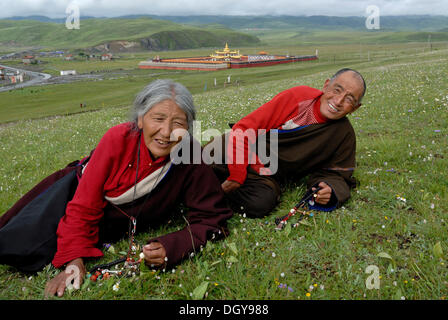 Vieille Femme tibétaine et l'homme en costume traditionnel tibétain couché dans un pré, derrière un monastère tibétain avec toits d'or et Banque D'Images