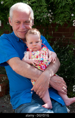 Petite fille de bébé étant tenue par son grand-père souriant, assis à l'extérieur dans le jardin Banque D'Images