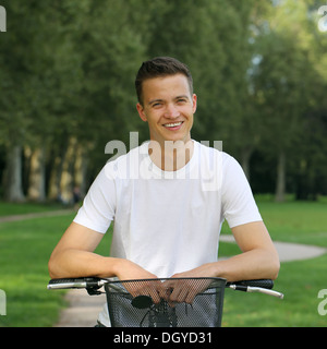 Smiling young man leaning against son vélo dans un parc Banque D'Images