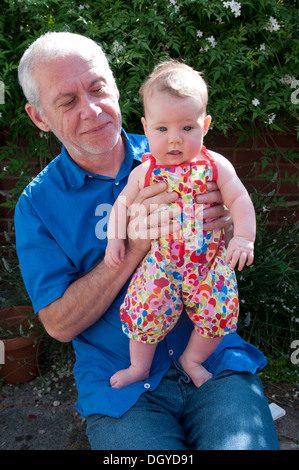 Petite fille de bébé étant tenue par son grand-père souriant, assis à l'extérieur dans le jardin Banque D'Images