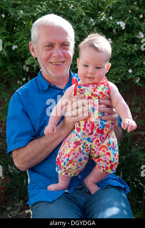 Petite fille de bébé étant tenue par son grand-père souriant, assis à l'extérieur dans le jardin Banque D'Images