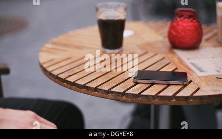 Téléphone mobile et un verre de café noir sur street cafe table avec un homme assis par Banque D'Images