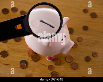 Une loupe magnifier la fente sur une tirelire, pièces autour d'elle Banque D'Images