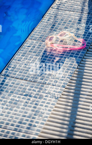 La lumière du soleil qui brille sur une paire de lunettes de natation sur le bord d'une piscine Banque D'Images