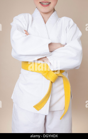 A smiling girl with arms crossed portant uniforme d'arts martiaux avec ceinture jaune Banque D'Images