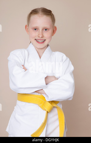 A smiling girl with arms crossed portant uniforme d'arts martiaux avec ceinture jaune Banque D'Images