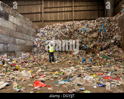 Usine de recyclage dans l'homme debout près de gros tas de matériau plastique séparés des déchets ménagers Banque D'Images