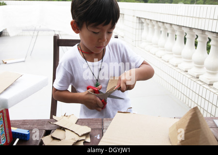 C'est une photo d'un petit garçon asiatique fait whi travail DIY avec du carton pour faire une fusée. Il coupe, colle et peintures. Il est pro Banque D'Images