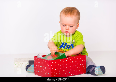 Un homme tout-petit enfant est l'ouverture des boîtes cadeaux de Noël sur fond blanc. Le garçon est d'origine ethnique caucasienne et entre 1 et 2 Banque D'Images
