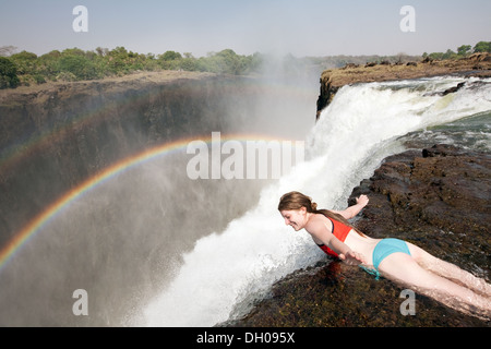 Une jeune femme accrochée au bord de la piscine des Devils, Victoria Falls, prise sur l'île Livingstone, Zambie Afrique - vacances d'aventure Banque D'Images