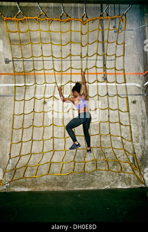 African American Woman climbing wall net in gym Banque D'Images