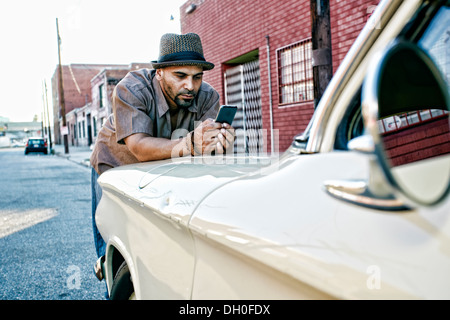 Hispanic man using cell phone on vintage car Banque D'Images