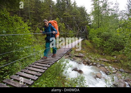 Femme, femme hiker with backpack crossing suspension bridge voyage Taja, près de la ville historique de Canyon, Pacific Northwest Banque D'Images