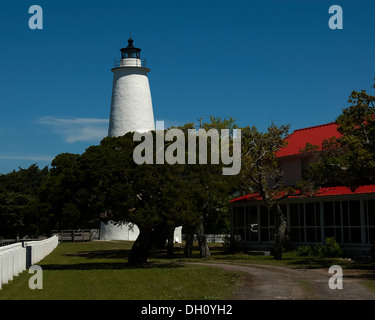 Ocracoke Island Lighthouse derrière les arbres avec la clôture blanche et du toit de la maison montrant. Banque D'Images