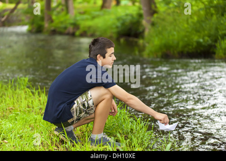 Garçon avec bateau de papier près de la rivière Banque D'Images