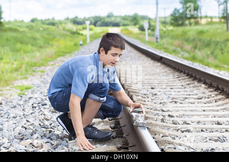 Garçon met des pierres sur des rails de chemin de fer Banque D'Images