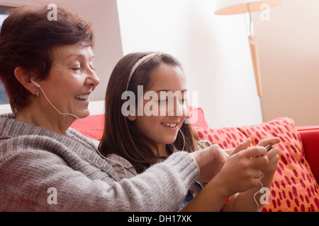 Older Hispanic woman listening to music with granddaughter Banque D'Images