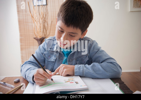 Hispanic boy doing homework at desk Banque D'Images