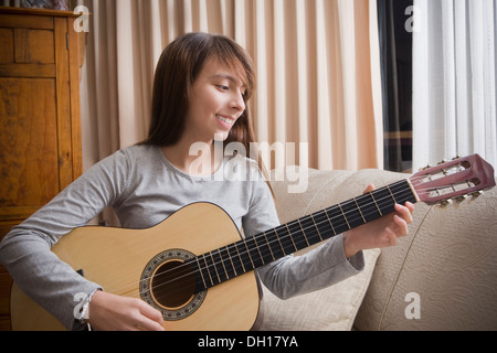 Young Girl playing guitar on sofa Banque D'Images