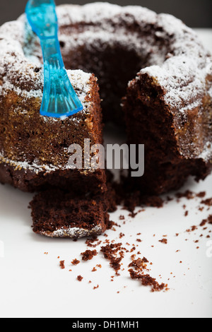 Gros plan du gâteau au chocolat à sec avec pièce découper saupoudrée de sucre glace et fourchette en plastique bleu Banque D'Images