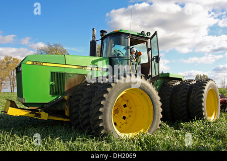 Un jeune garçon se penche par la porte d'un grand tracteur John Deere Roue triple comme ses rides dans la cabine avec son grand-père Banque D'Images