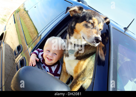 Un mignon, smiling baby boy et son chien berger allemand sont traîner une fourgonnette fenêtre sur un jour d'été Banque D'Images