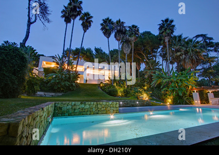 Palmiers et piscine éclairée en début de soirée dans le jardin d'une villa moderne dans le sud de l'Espagne Banque D'Images