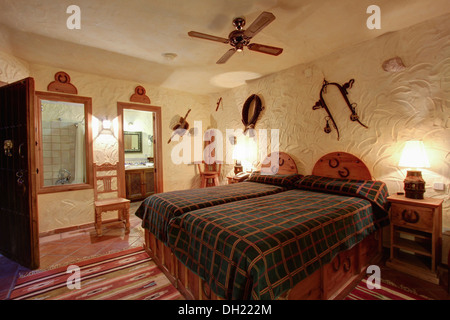 Bouilloire ventilateur de plafond au-dessus de lit en bois avec couvercle marron vérifié en espagnol chambre avec des murs texturés et porte de salle de bains Banque D'Images