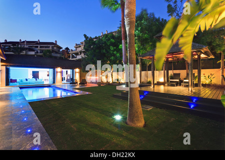 Palmier en pelouse à côté grande terrasse en bois et piscine dans jardin de Villa éclairée la nuit Banque D'Images