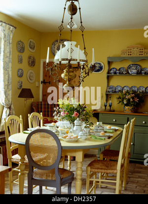 Laiton verre +lampe victorienne crème au-dessus de table et chaises pour déjeuner ensemble en jaune pâle vert cottage salle à manger avec buffet Banque D'Images