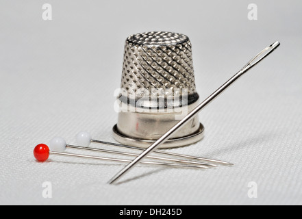 Aiguille à coudre, épingles et virole allongée sur tissu en lin blanc Banque D'Images