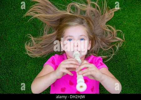 Enfants Enfant blonde girl playing flute lying on grass pelouse arrière Banque D'Images