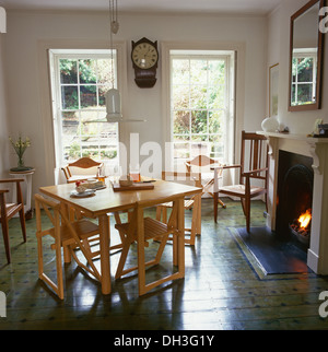 Table en bois clair, simple et de chaises pliantes en salle à manger avec marbre vert peint décorative et d'une cheminée avec feu allumé Banque D'Images