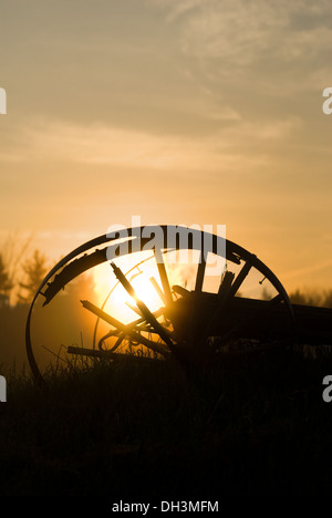 Le soleil se lève derrière un volant cassé gisant dans un champ de foin. Banque D'Images