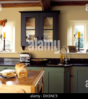 Placard à façade en verre au-dessus du pain sur le plan de travail dans la  petite cuisine avec de la vaisselle sur l'étagère au-dessus de casseroles  en rack mural en bois Photo